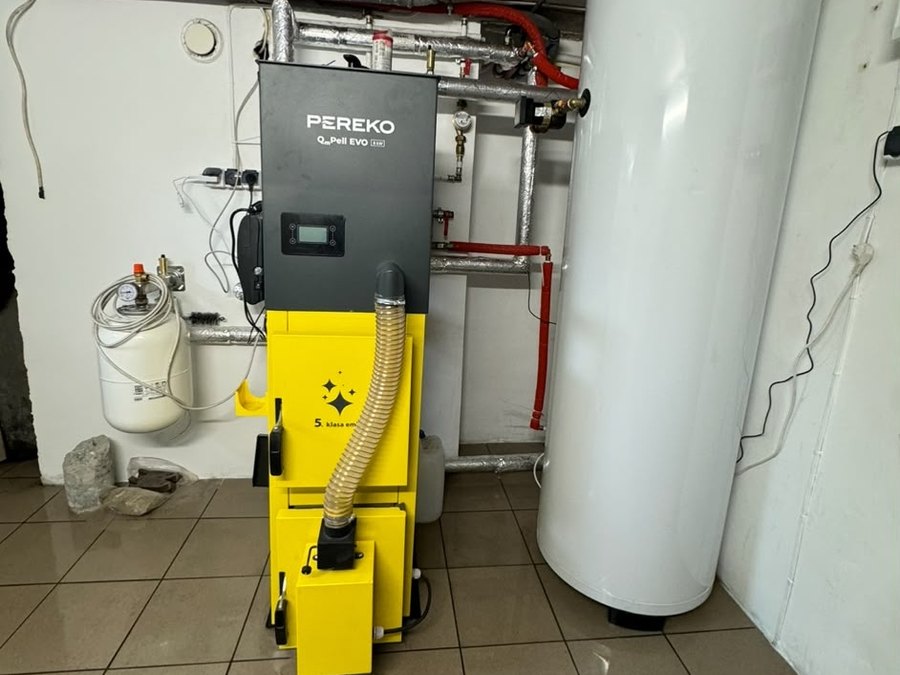 Żółty kocioł Pereko na pellet obok podgrzewacza wody